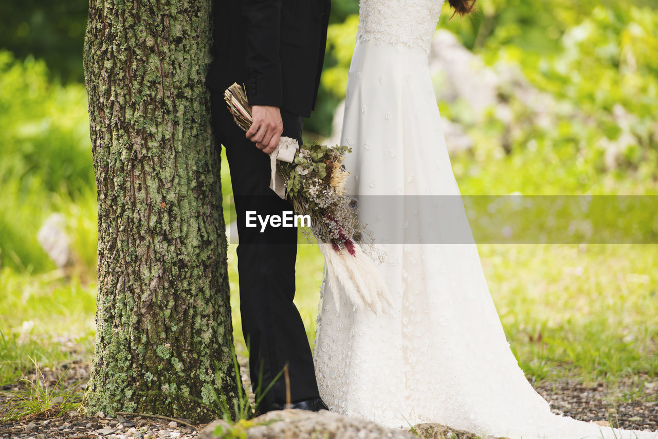 Midsection of couple standing by tree trunk