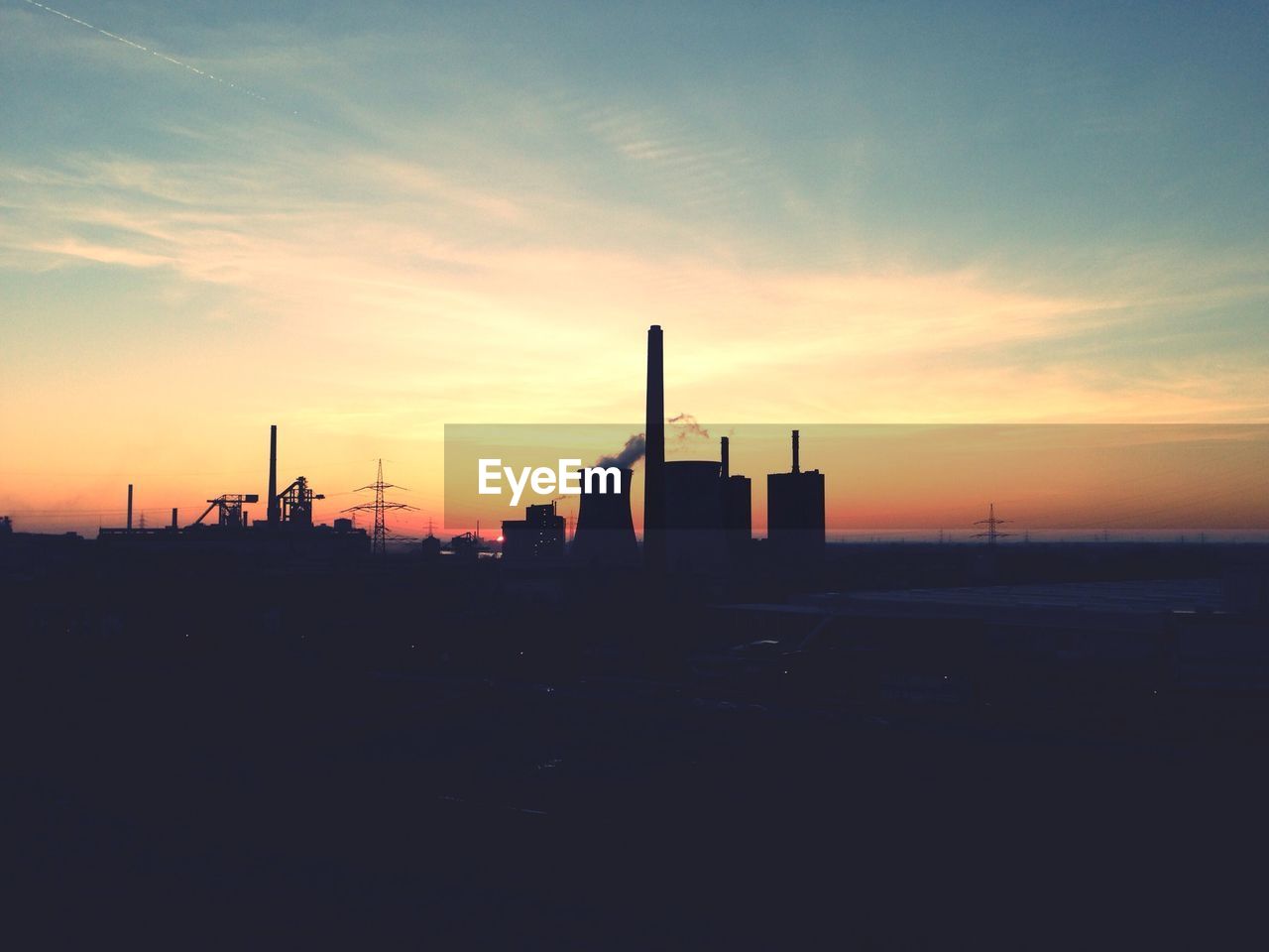 Smoke emitting from silhouette chimney against cloudy sky during sunset