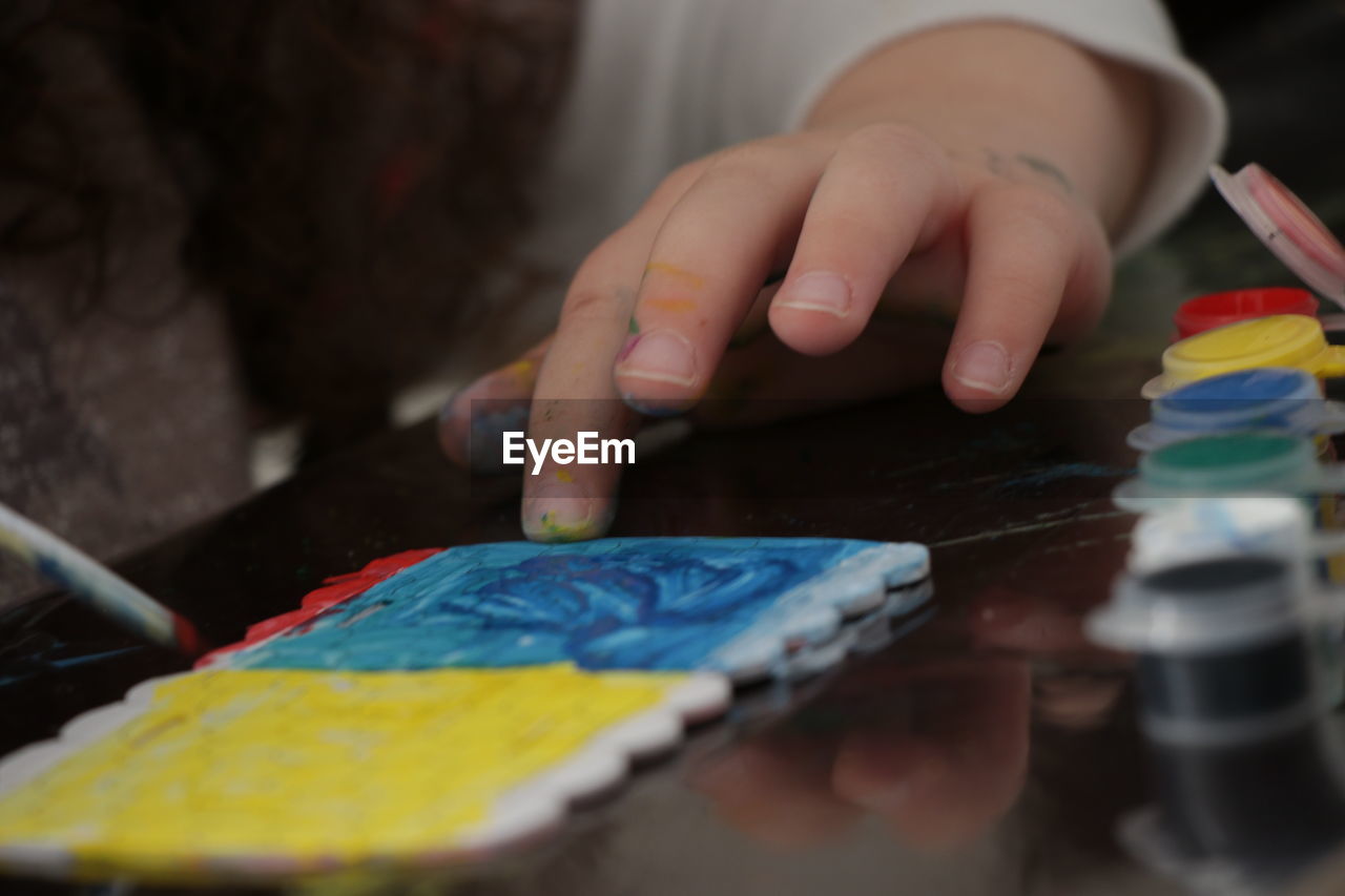 Cropped hand of girl painting tile on table