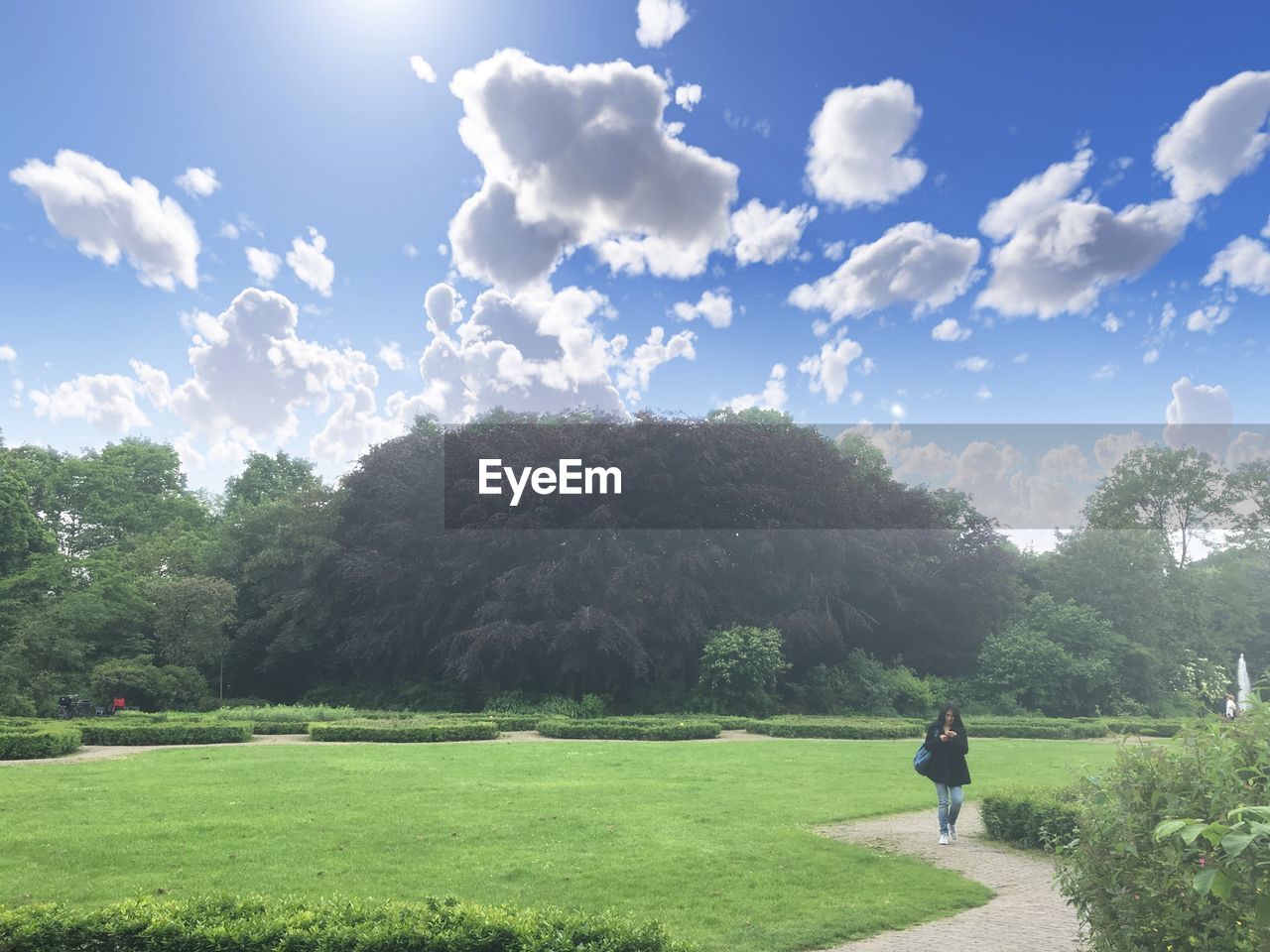 Woman walking on footpath by grassy field against trees at park