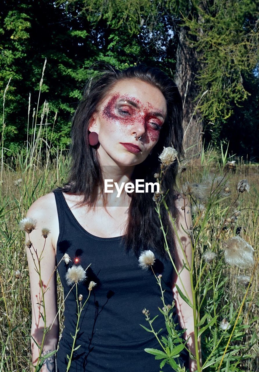 Portrait of woman with glitter make-up standing by plants on field