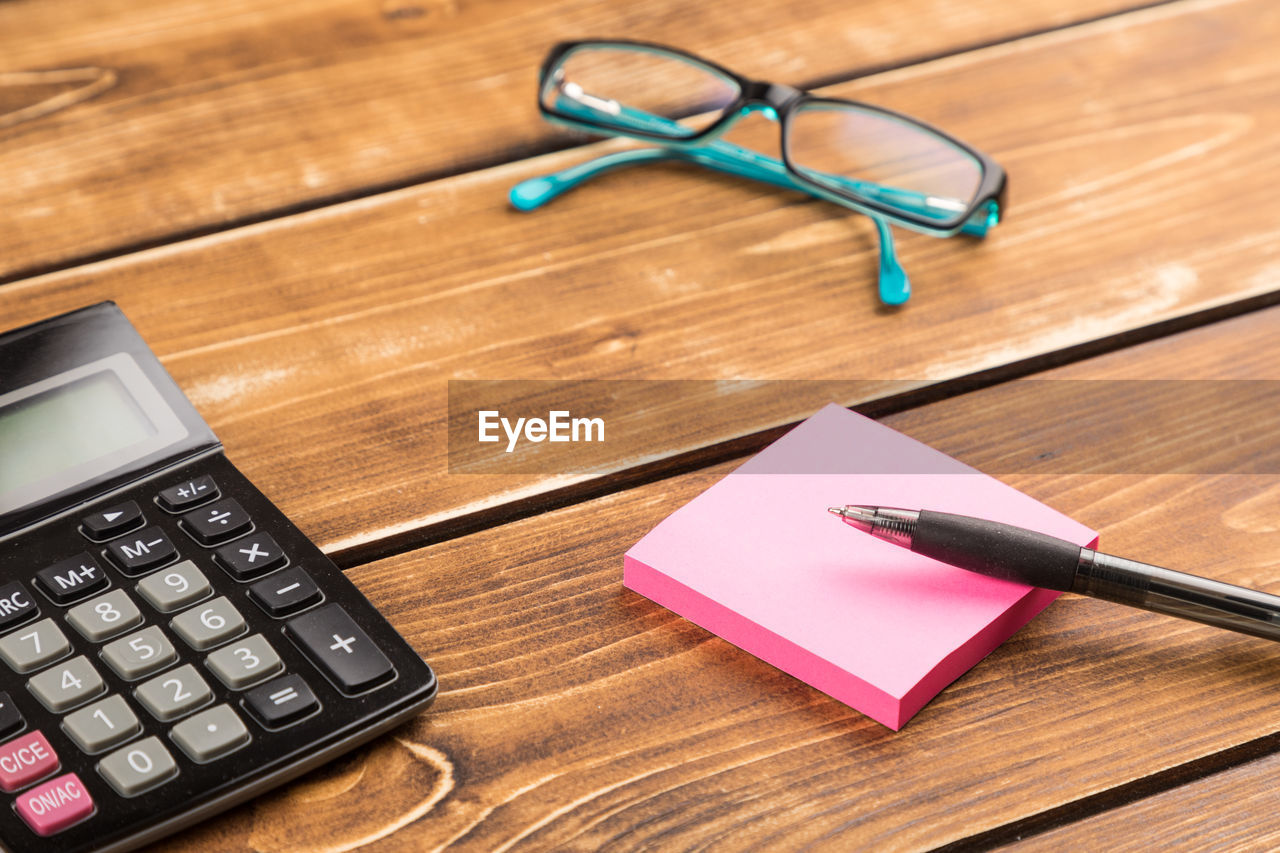 High angle view of pen with adhesive notes and calculator on wooden table