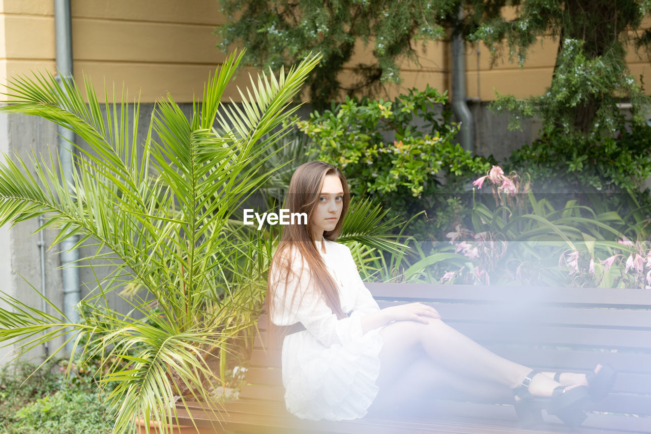 Full length portrait of young woman sitting on bench at park