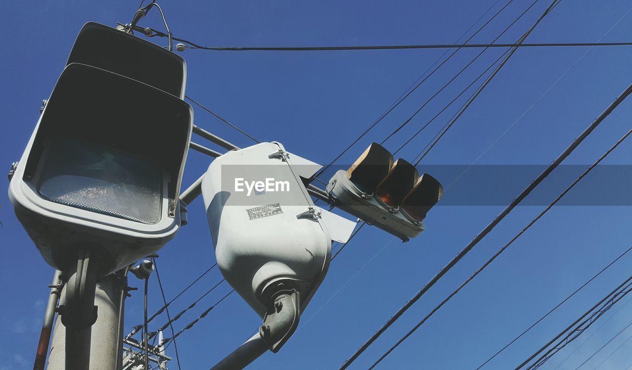 Low angle view of traffic light and power lines against clear blue sky