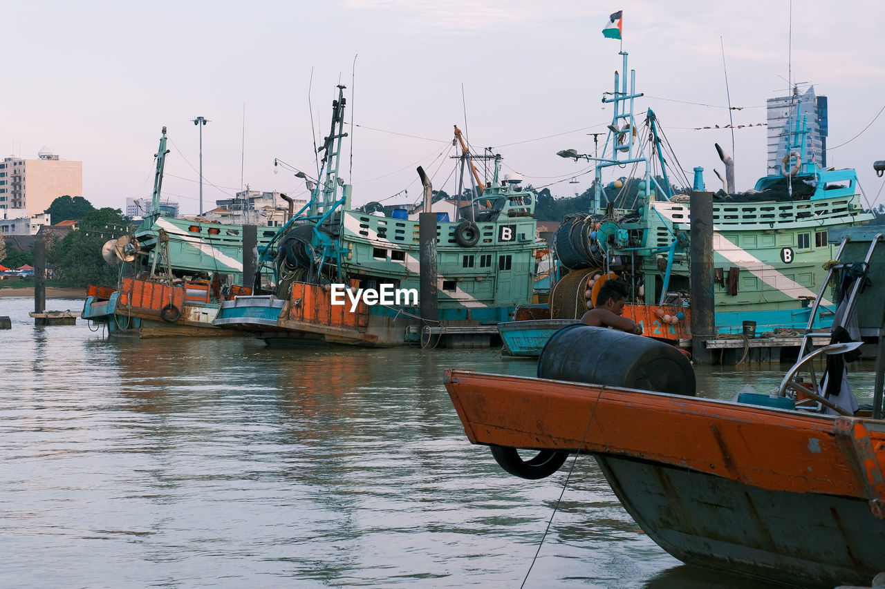 Fishing boats moored at harbor against sky