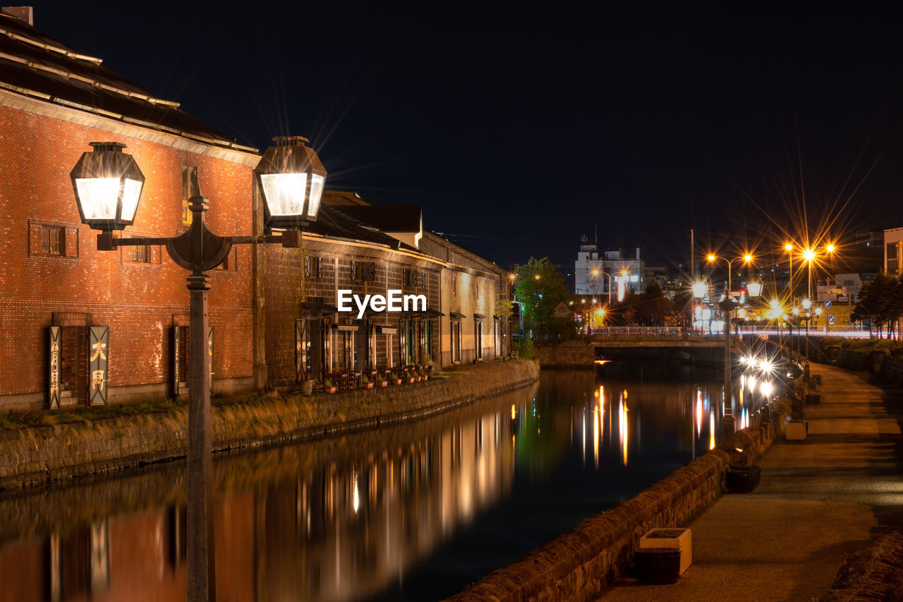 Illuminated street by river and buildings at night