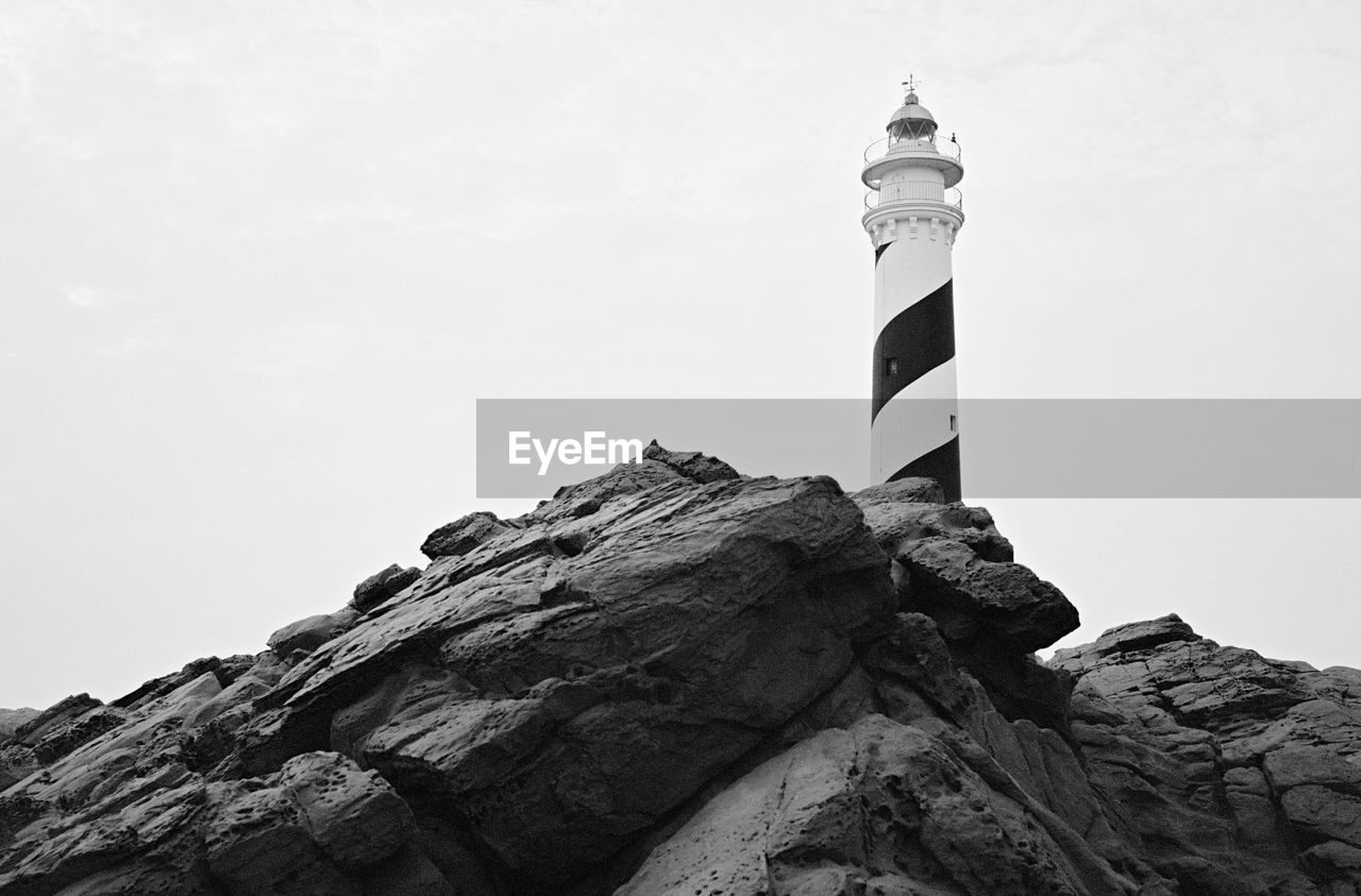 Low angle view of lighthouse on rock by building against sky
