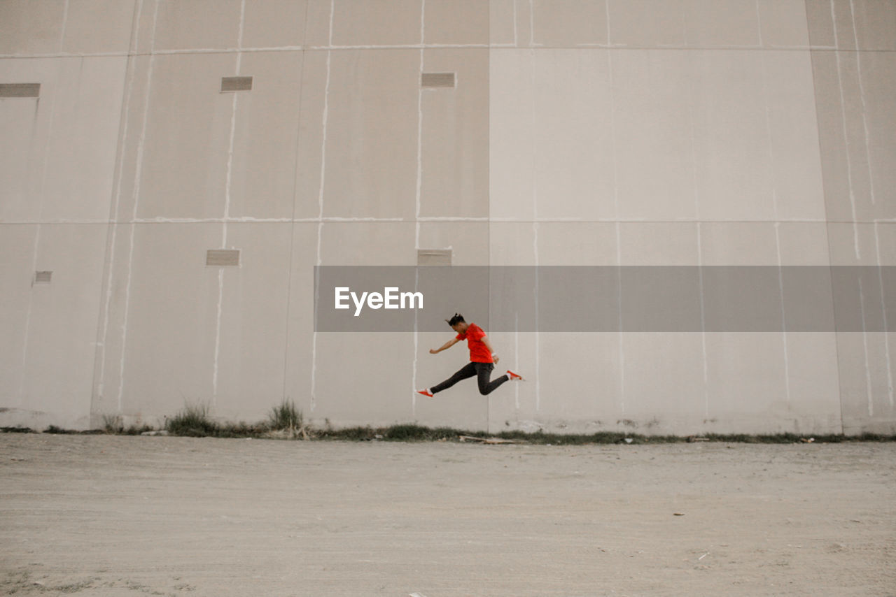 Side view of man jumping over ground against building