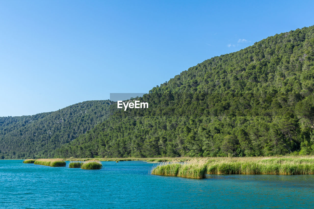 Scenic view of lake and mountains against clear blue sky