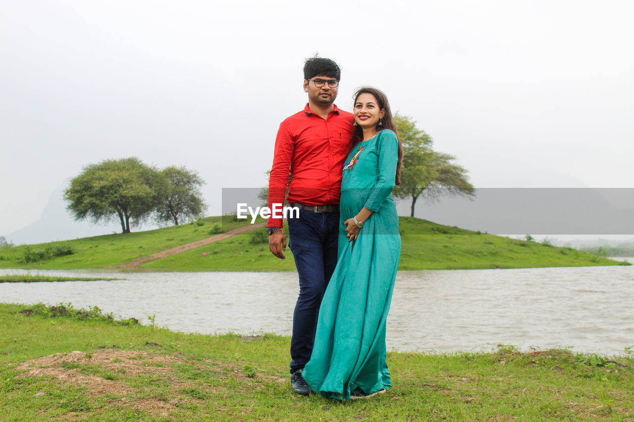 Portrait of young man standing with pregnant woman by river