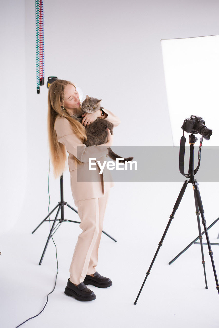 low angle view of woman holding camera against white wall at home