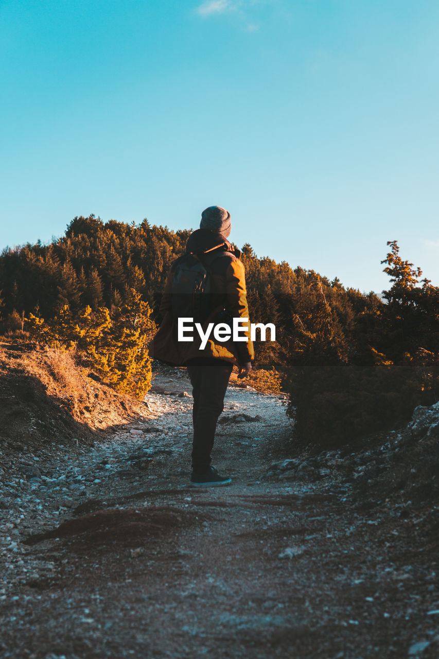 Rear view of woman standing on footpath against clear sky