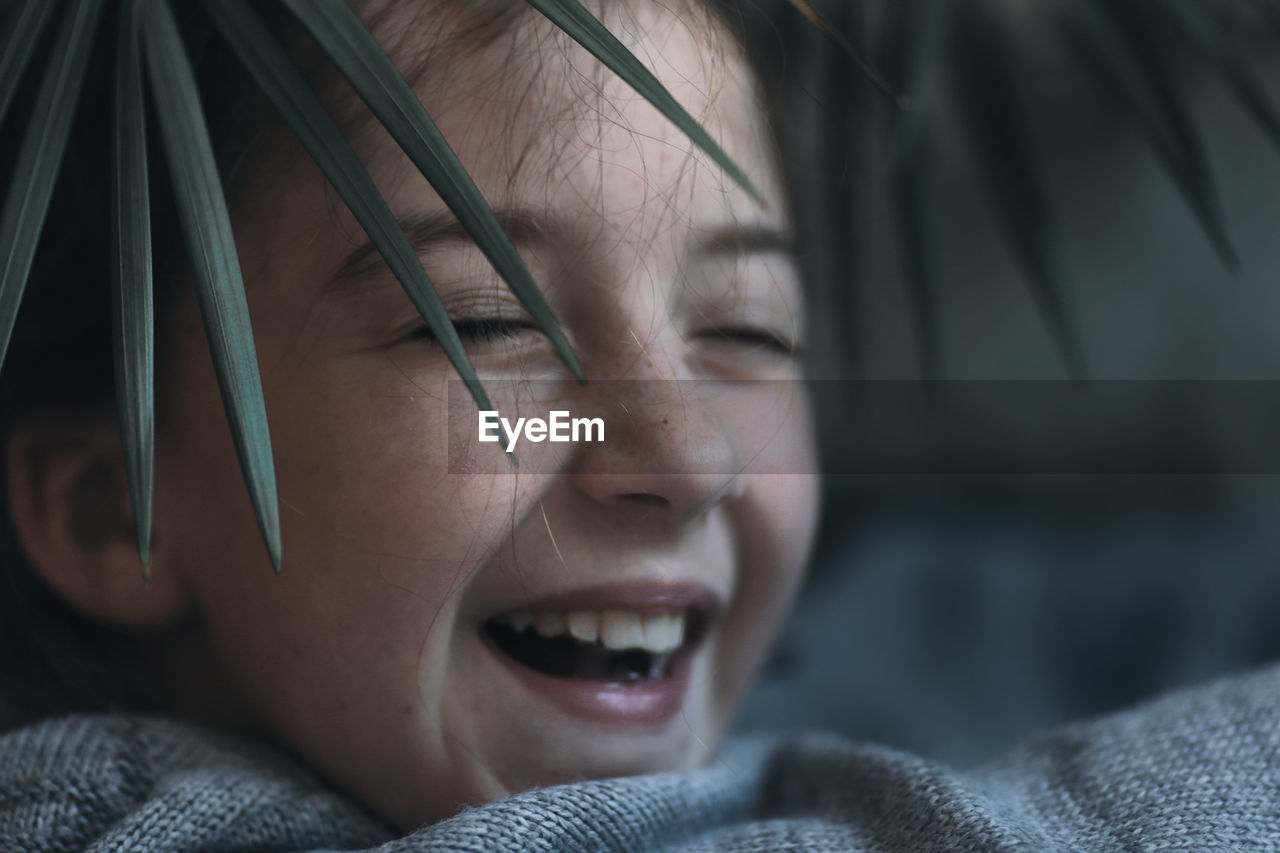 A cheerful child, a charming girl's face looking through the leaf of the plant.