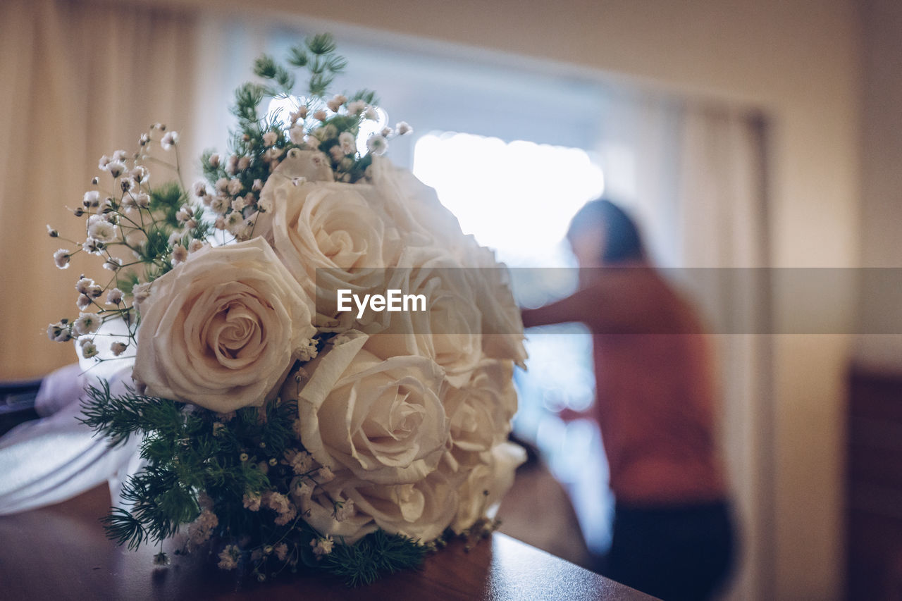 Close-up of rose bouquet on table against woman at home