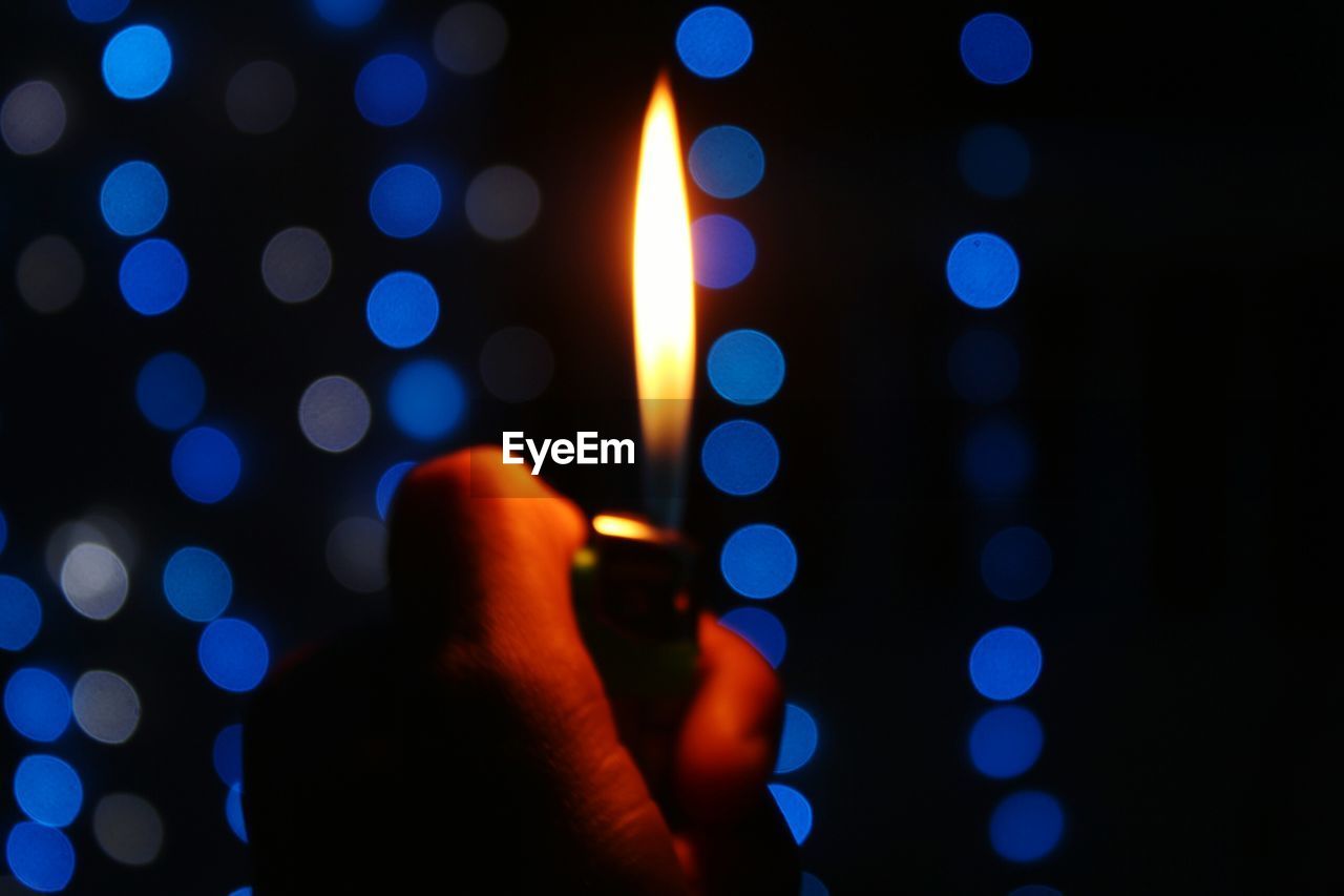 Close-up of hand holding illuminated cigarette lighter at night