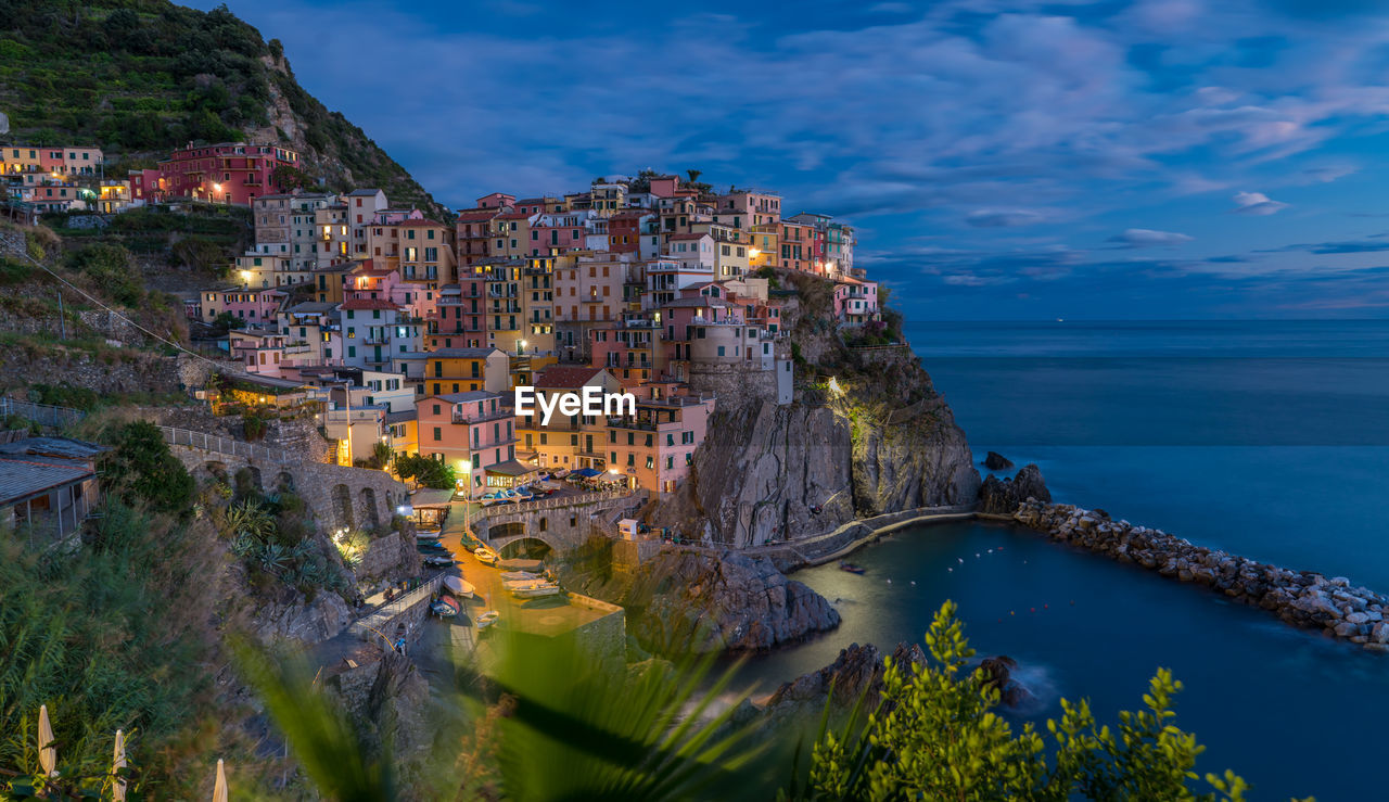 High angle view of illuminated buildings by sea against sky