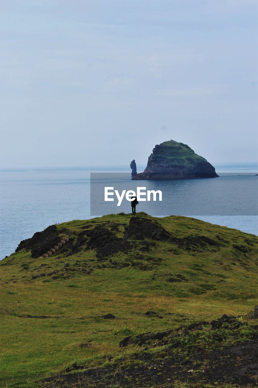 Woman standing on cliff by sea against sky