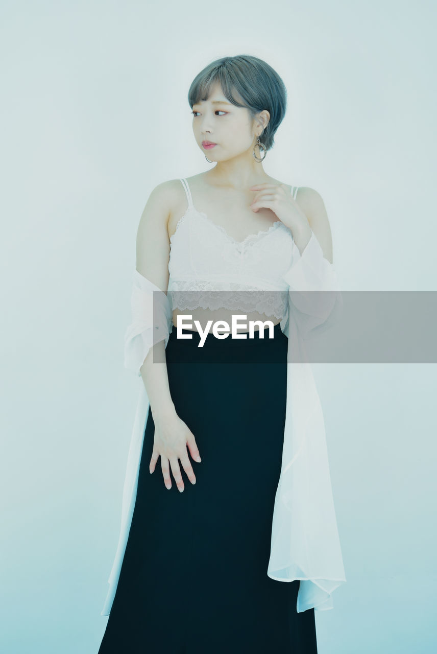 Portrait of young woman standing against white background