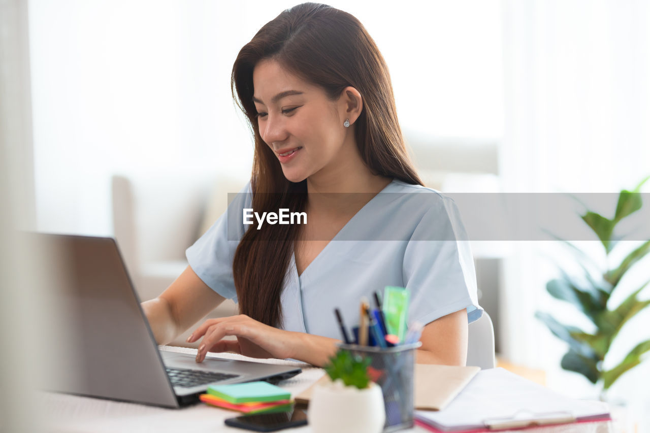 YOUNG WOMAN USING MOBILE PHONE IN LAPTOP