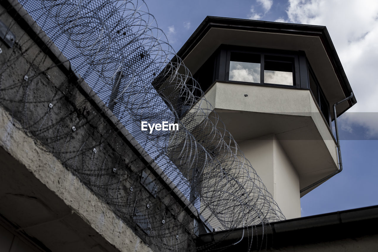 Low angle view of lookout tower by barbed wire fence against sky