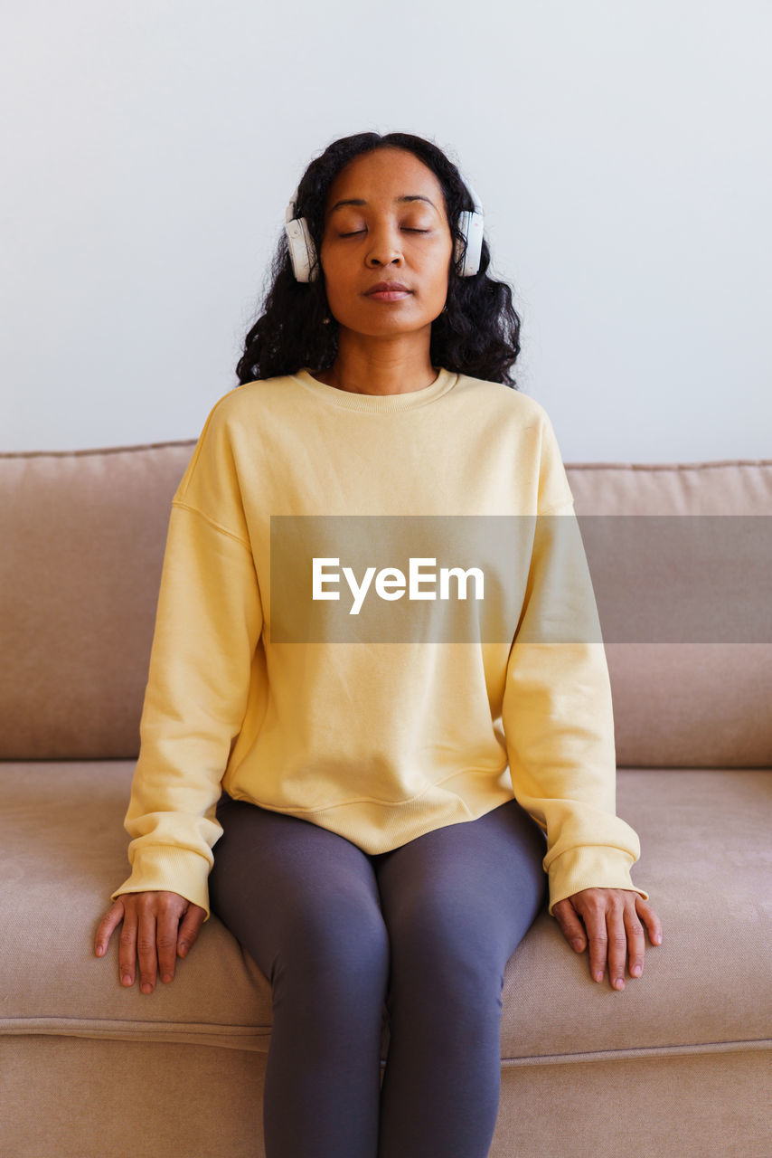 African-american female sitting on couch and listening to music in headphones. breathing therapy