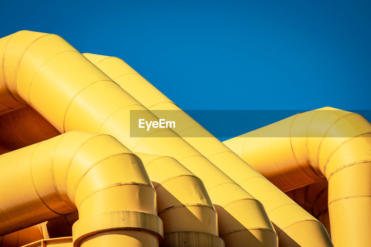 Low angle view of yellow pipes against clear blue sky