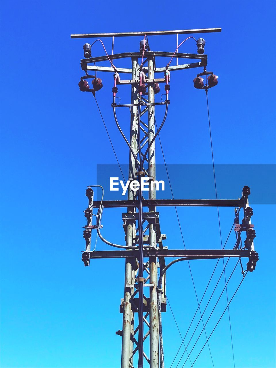 Low angle view of electricity pylon against blue sky