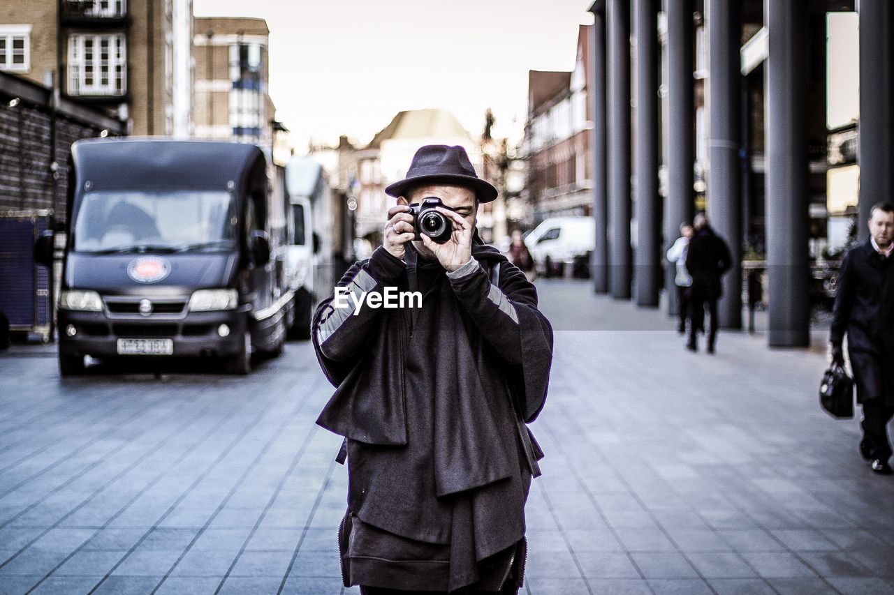 Man wearing hat photographing while standing in city