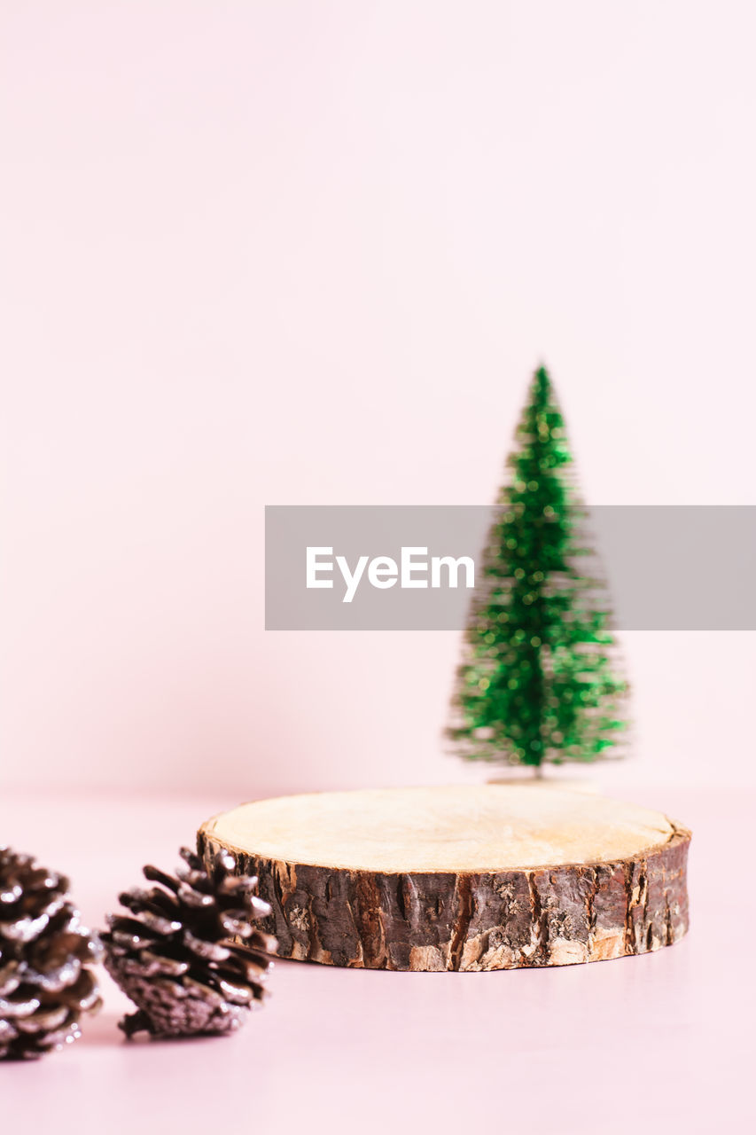 Wood cut podium, decorative christmas tree and pine cones on a pink background vertical view