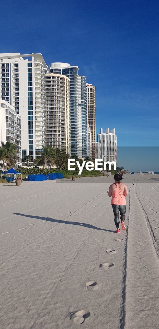 Rear view of woman running on sand at beach in city