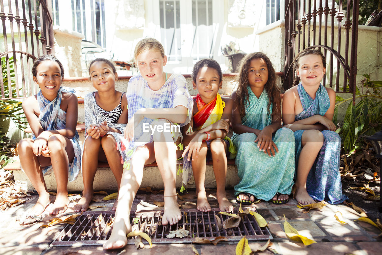 Portrait of female friends sitting side by side on steps against house