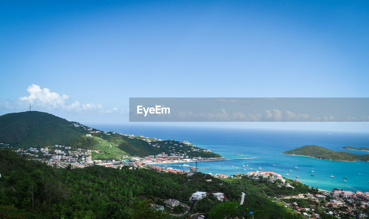 Aerial view of townscape by sea against blue sky