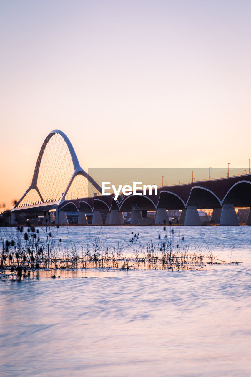 Arch bridge over river against sky during sunset