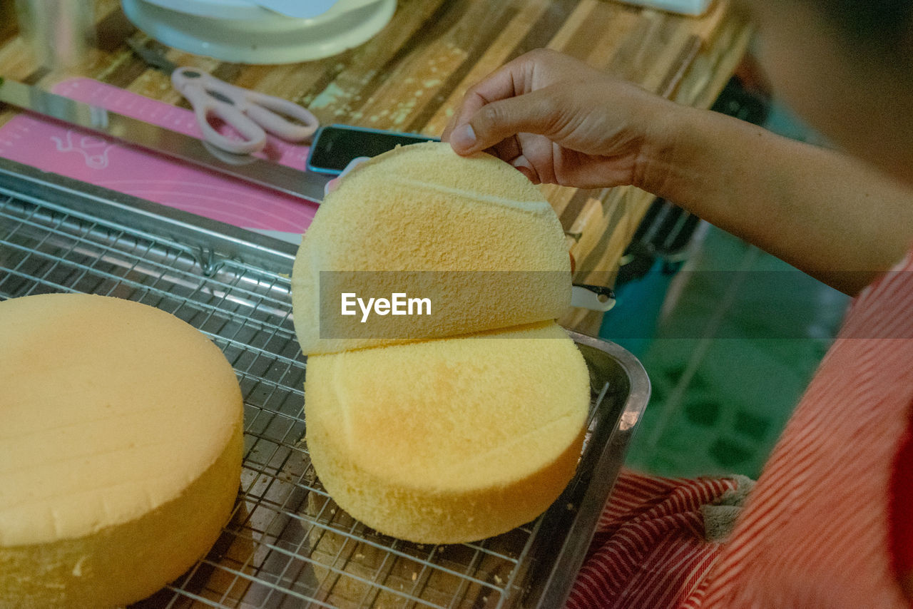 baked, hand, food, food and drink, one person, adult, indoors, women, freshness, holding, sweet food, business, occupation, breakfast, close-up, store, business finance and industry, working, small business, icing, retail, produce, dessert, yellow, sweet, high angle view, sweetness