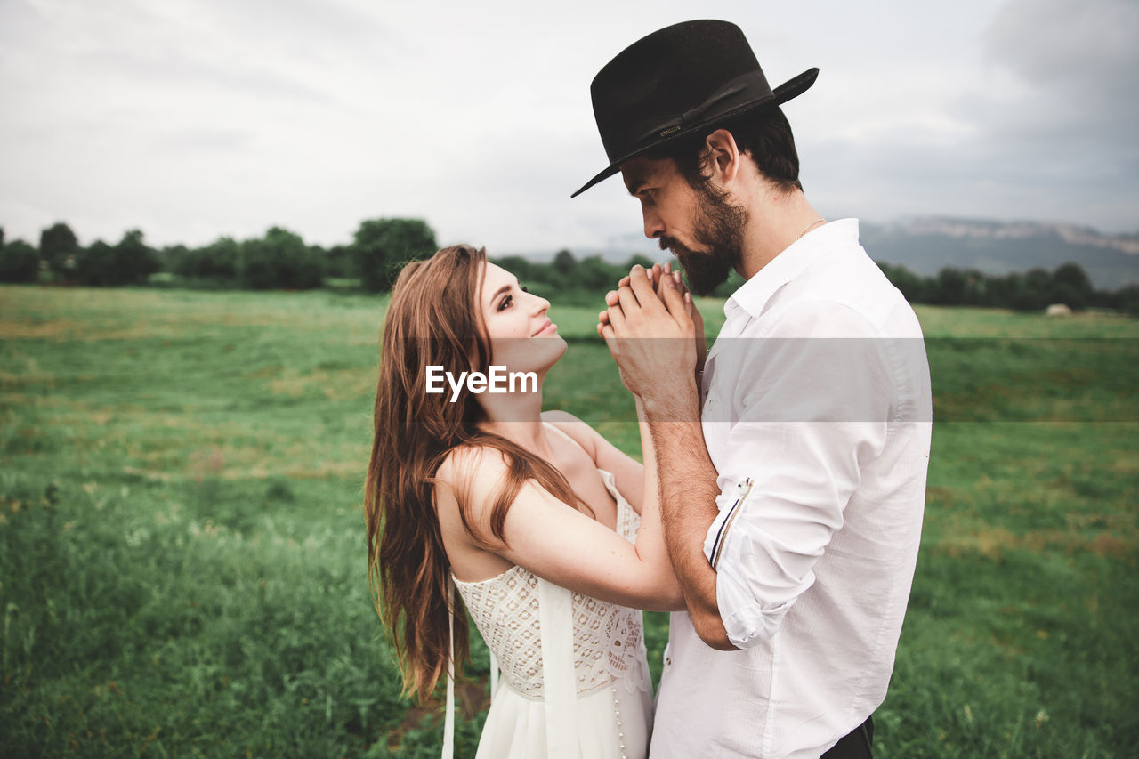 Side view of young couple holding hands while standing on field