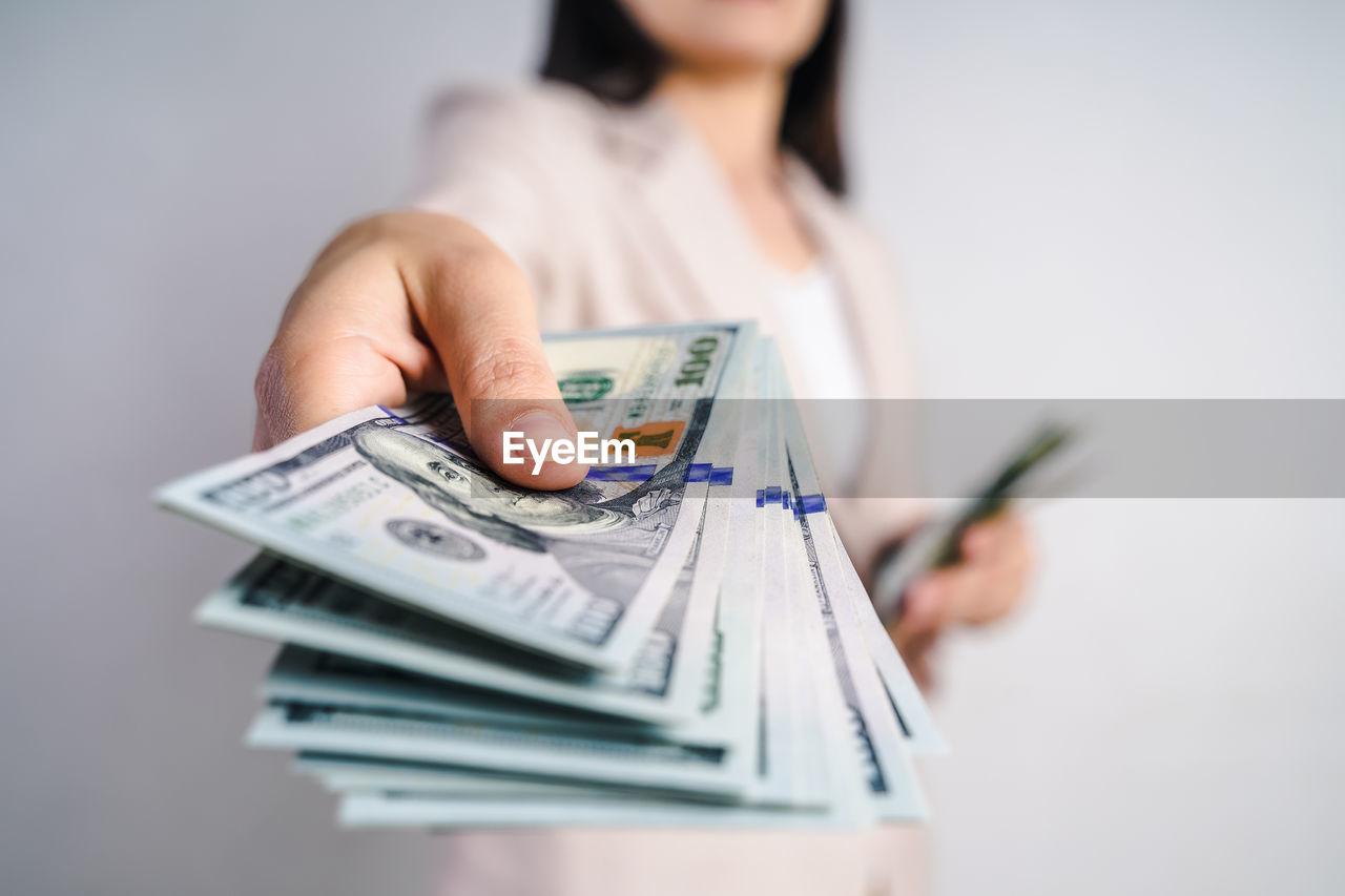 Midsection of woman holding paper currency against white background