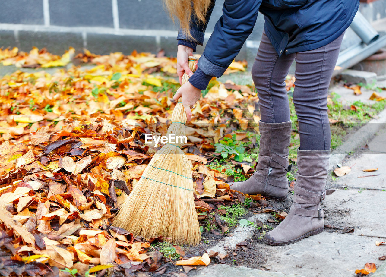 Low section of woman cleaning autumn leaves by sidewalk