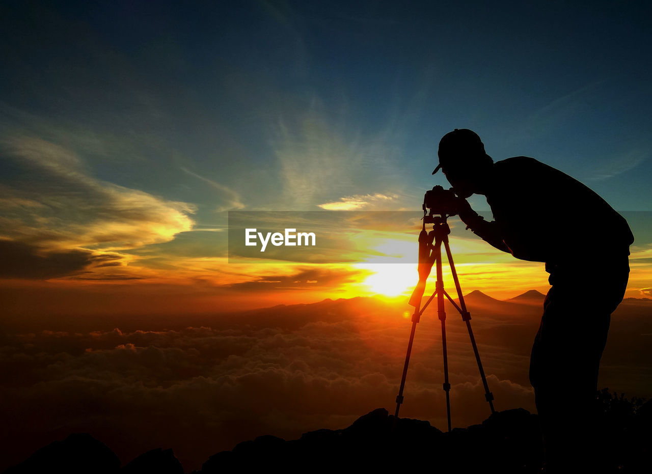 Silhouette man photographing against sky during sunset