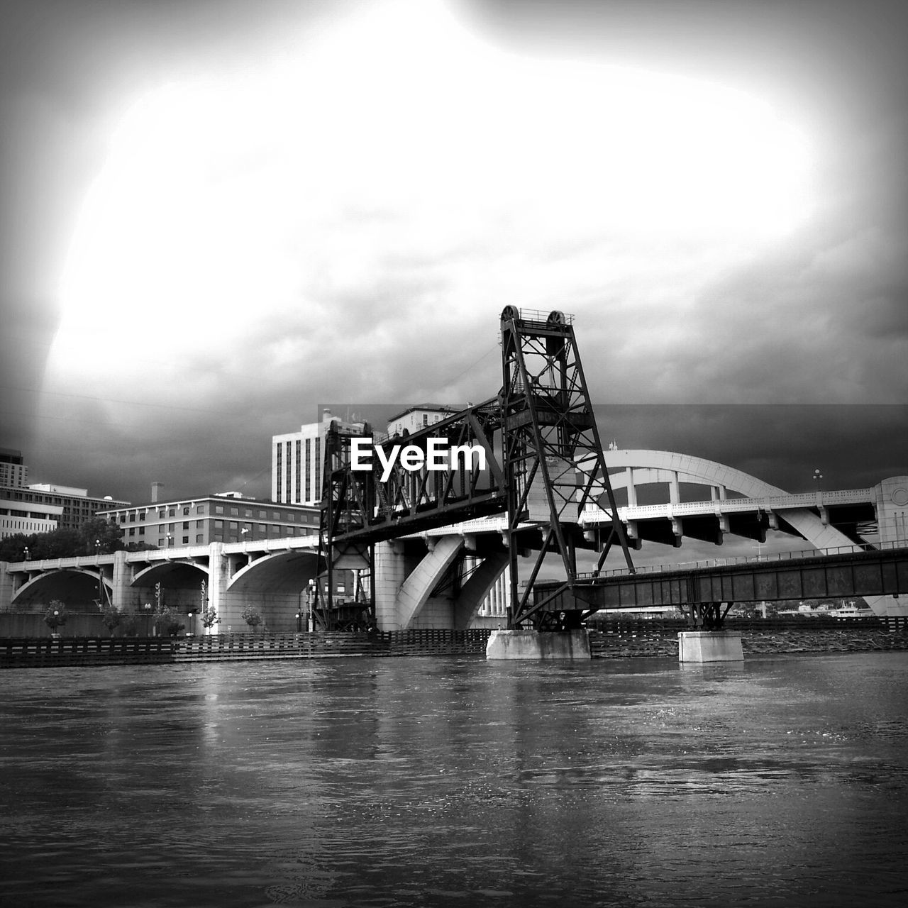 Bridge over river by buildings against cloudy sky