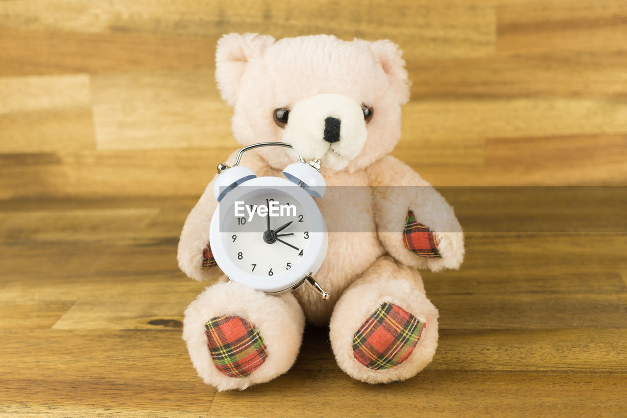 Close-up of alarm clock with teddy bear on hardwood floor