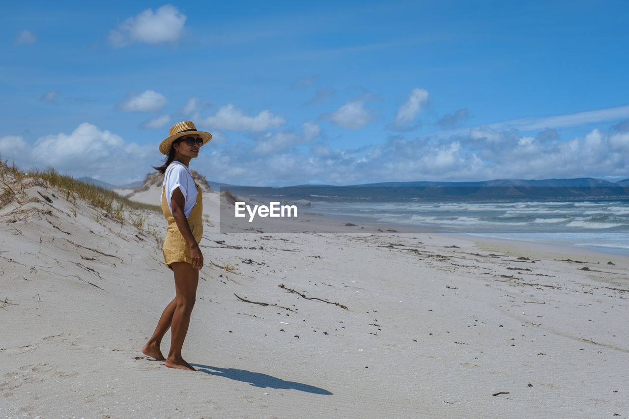 Side view of woman standing at beach against sky