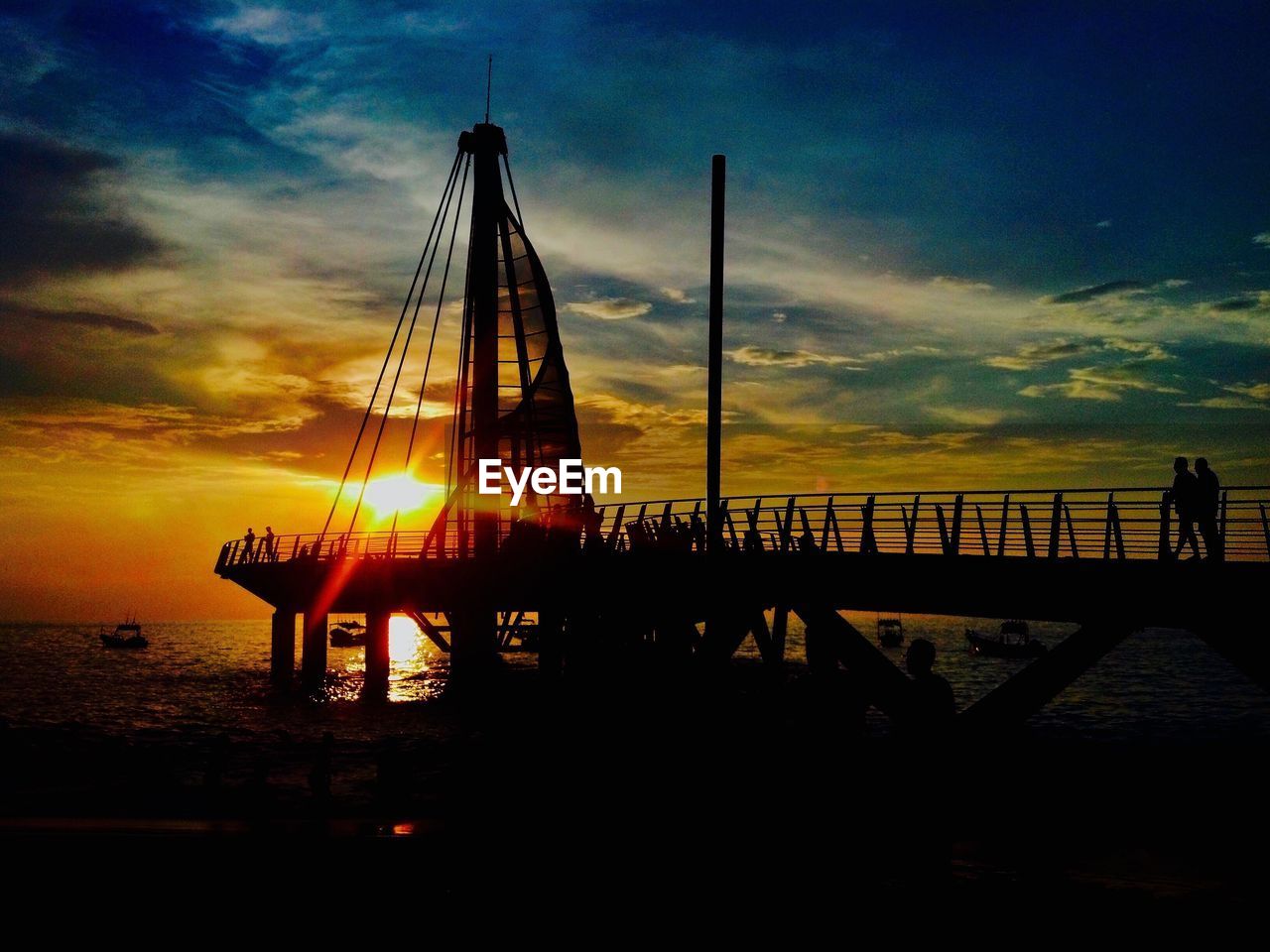 SILHOUETTE OF SUSPENSION BRIDGE AGAINST SKY AT SUNSET