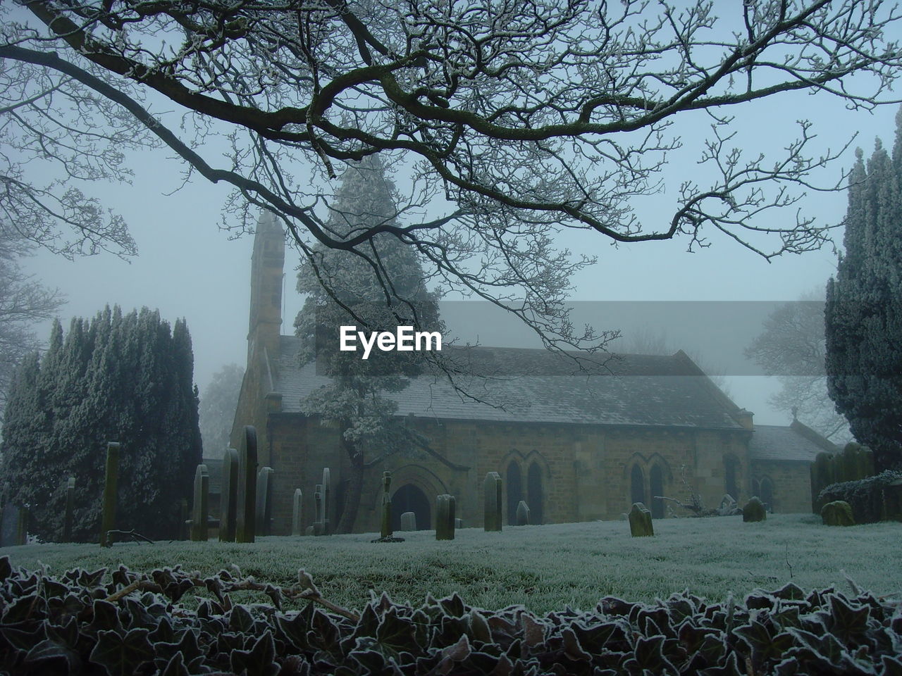 Church and cemetery against sky in foggy weather