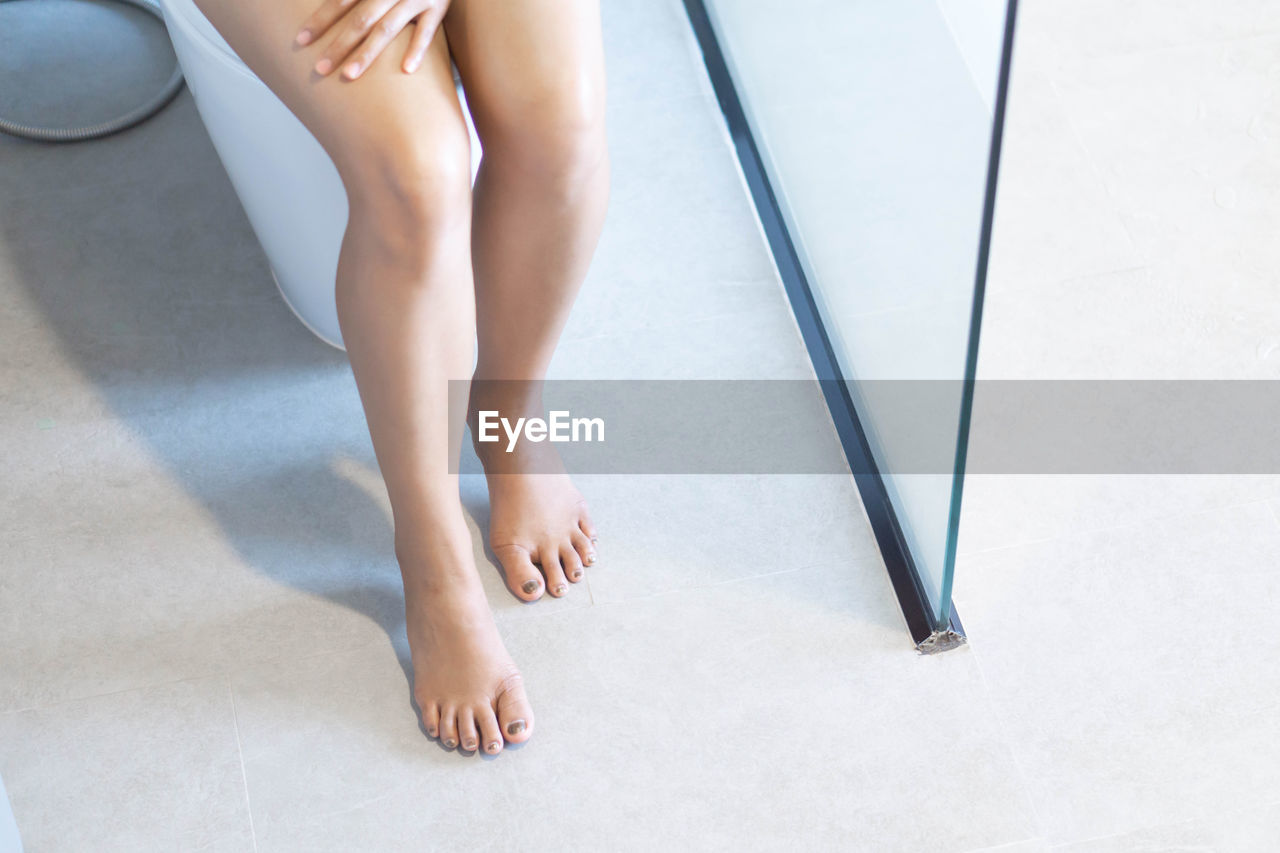 Low section of woman sitting in toilet on home