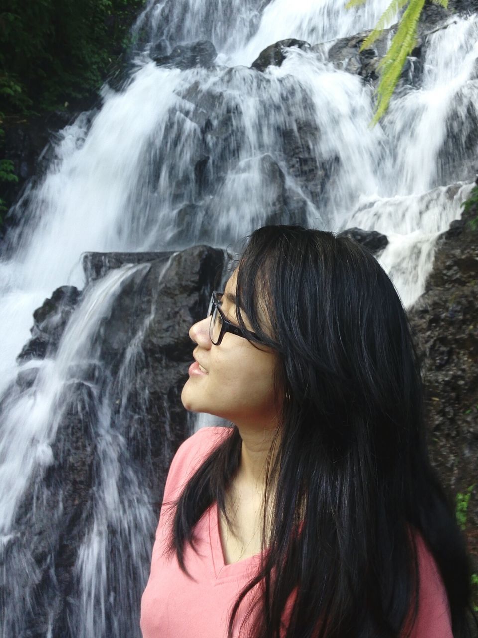 Smiling woman with long hair standing against waterfall