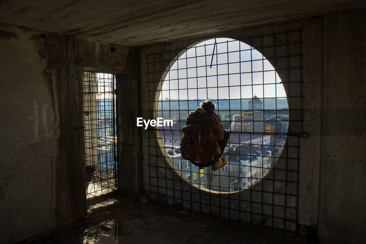 Rear view of man hanging on circular window against sky