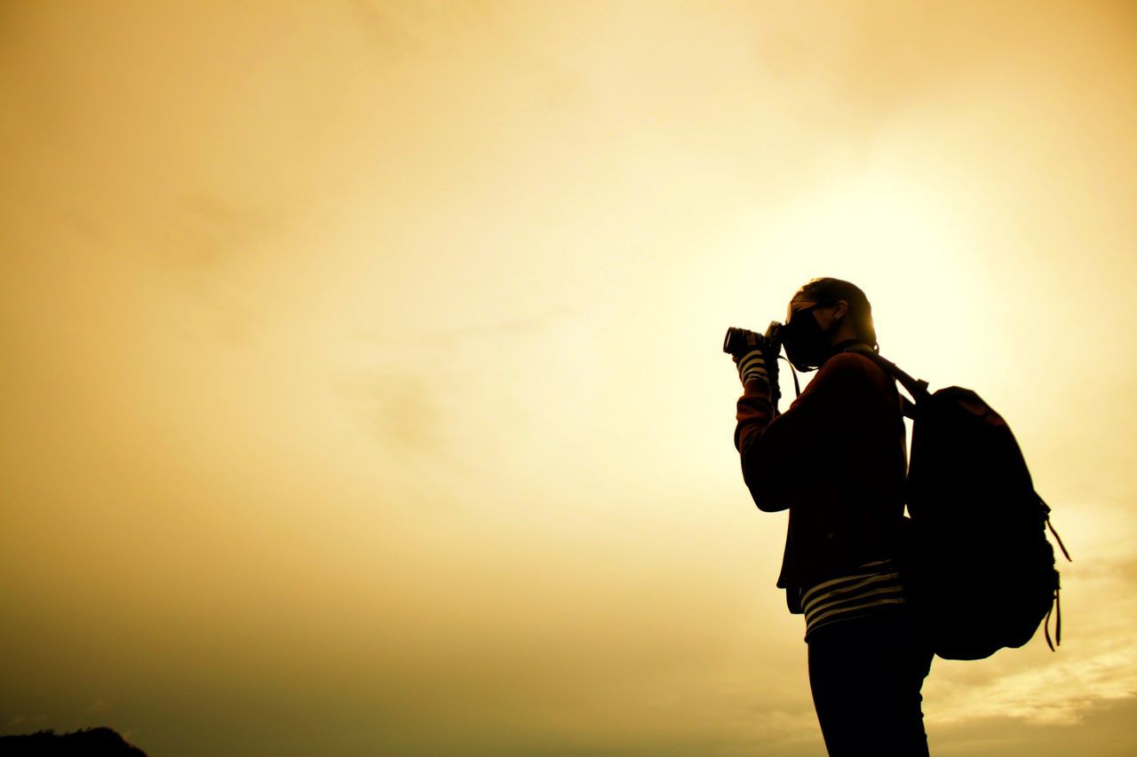 Low angle view of woman photographing through camera during sunset