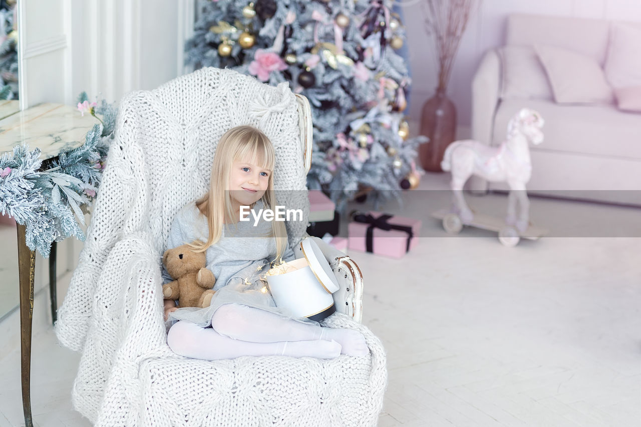 Cute girl looking away while sitting with toy on chair at home