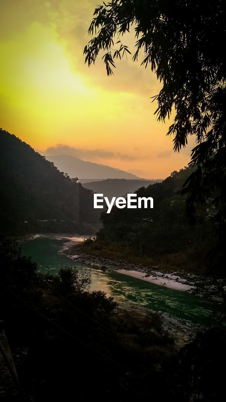 SCENIC VIEW OF RIVER BY SILHOUETTE MOUNTAINS AGAINST SKY AT SUNSET