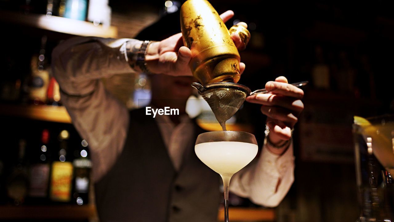 Bartender pouring liquid from shaker into cocktail glass